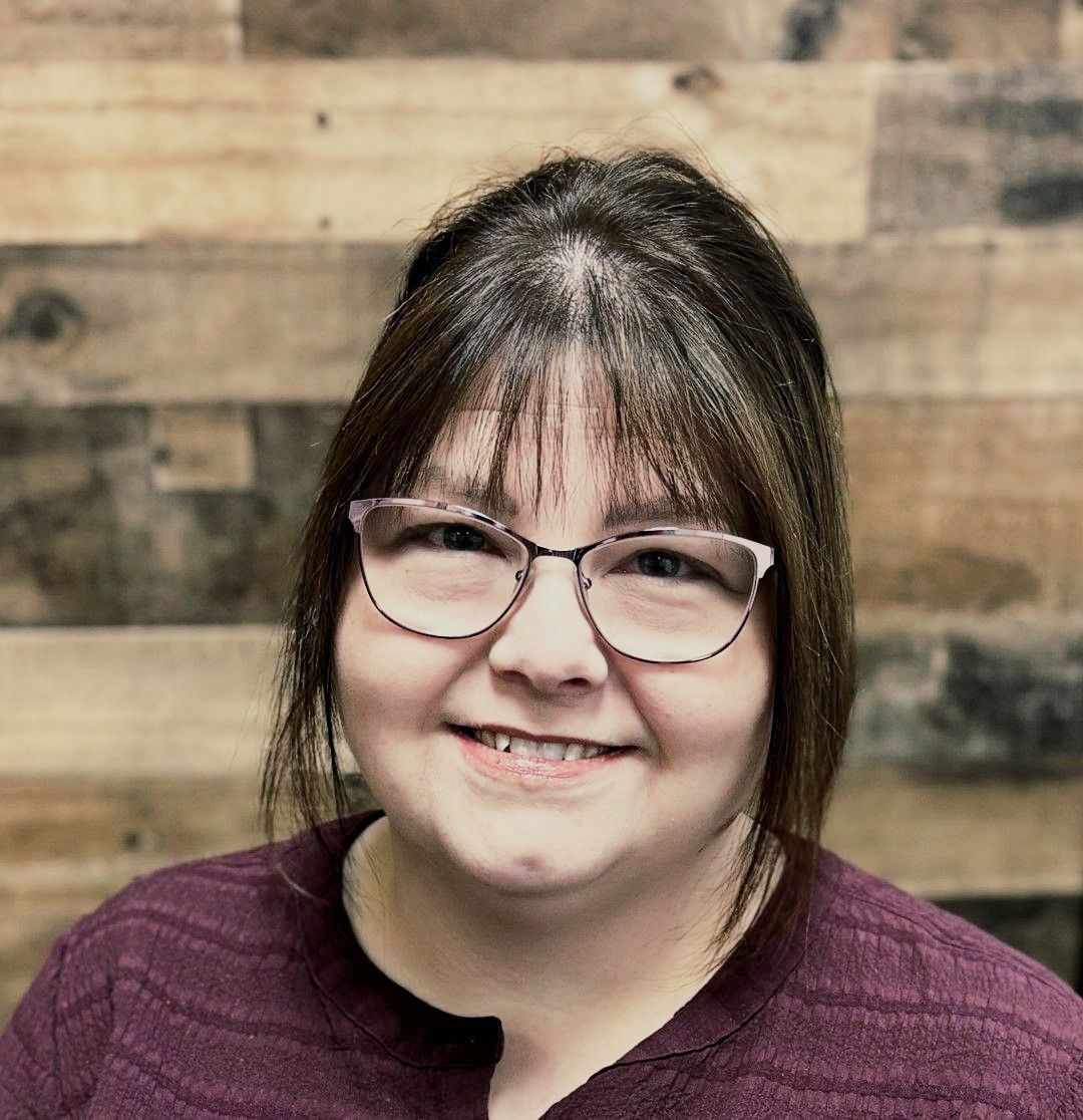 A woman wearing glasses and a purple shirt is smiling for the camera.