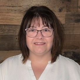 A woman wearing glasses and a purple shirt is smiling for the camera.