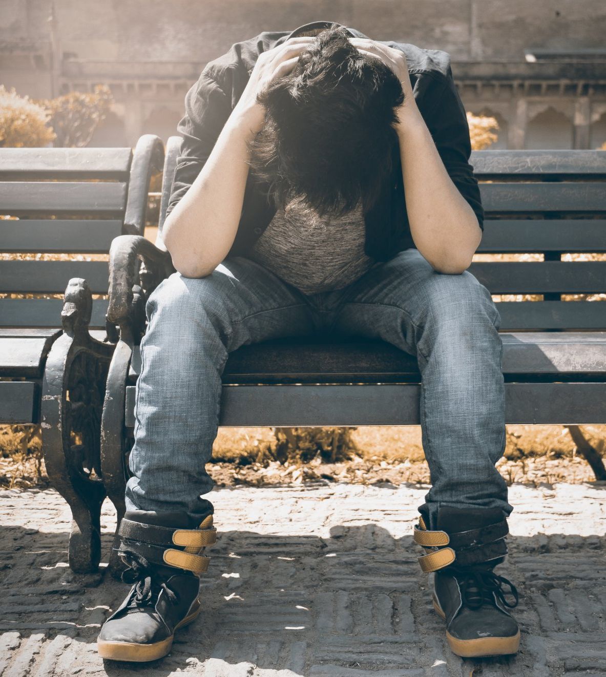 teenager on park bench with head in hands