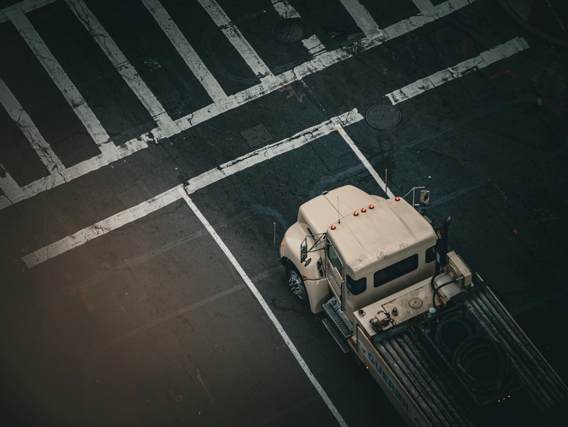 Tan truck parked on dark asphalt with white crosswalk lines. Aerial view.