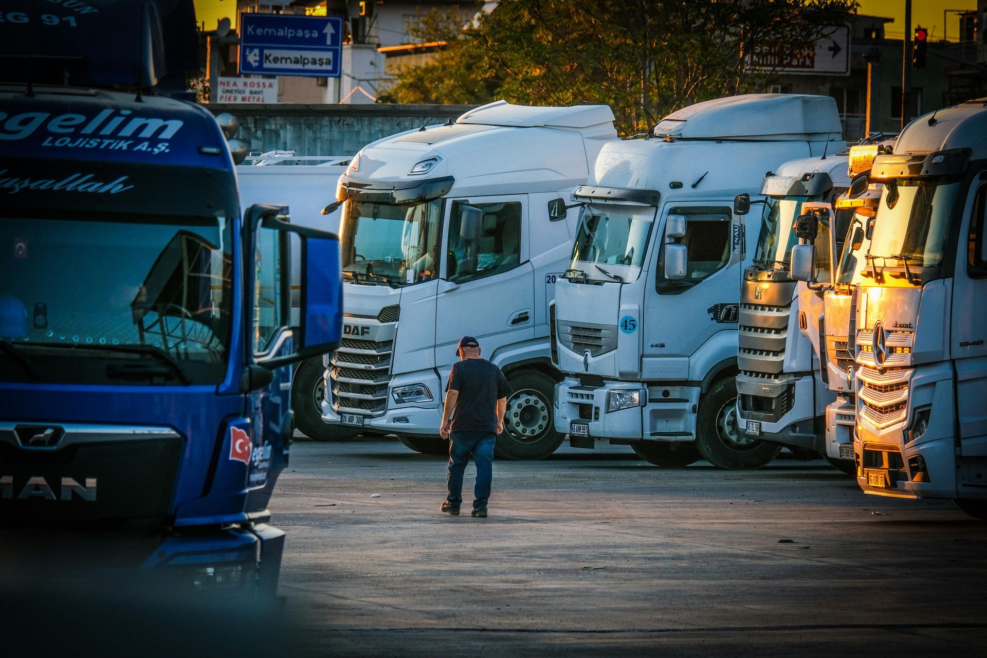 Trucks parked in a lot, a person in dark clothing walks toward them, setting sun.
