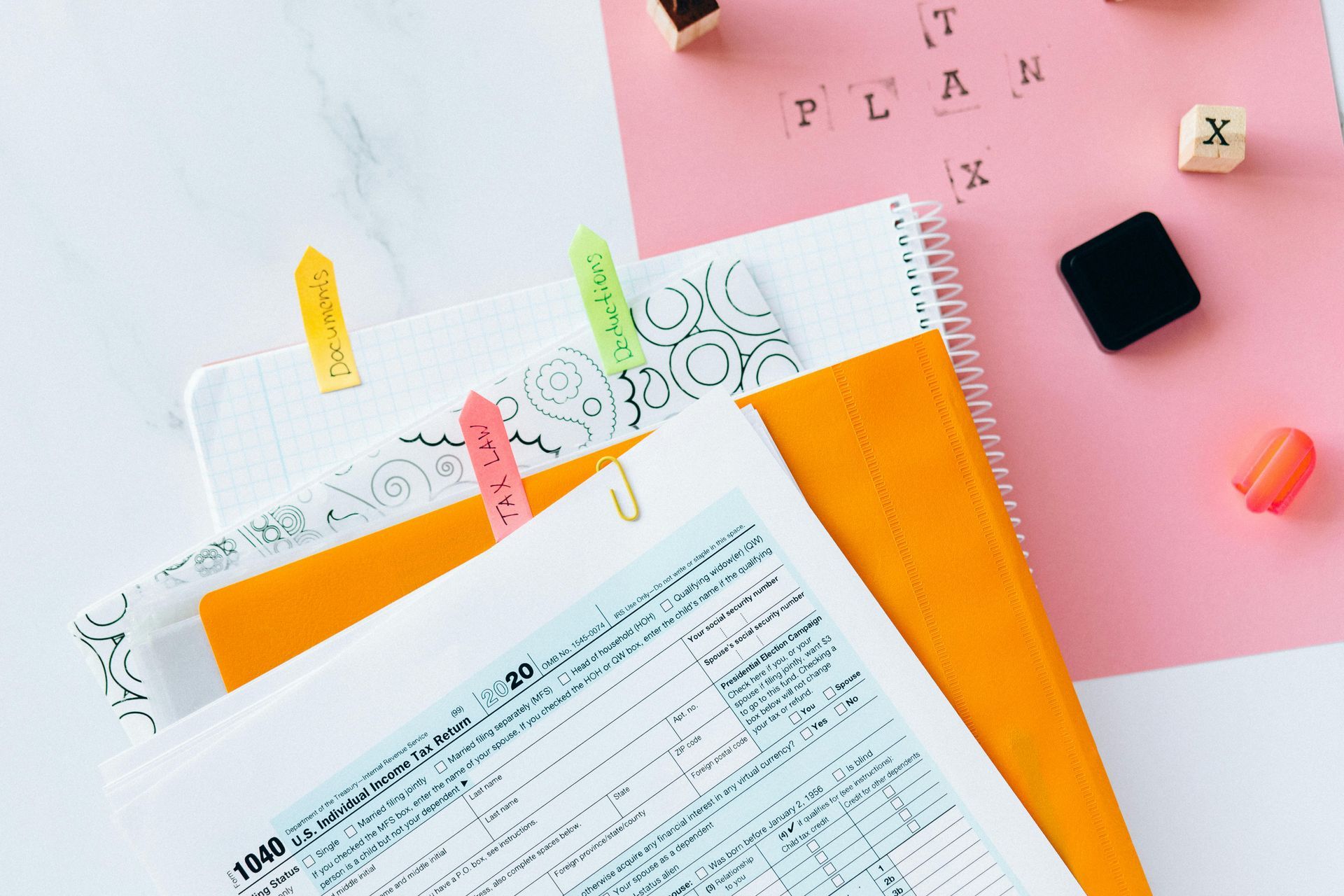 Assorted notebooks, papers, and accessories arranged on a white surface, including colorful sticky notes and a pink paper with the word