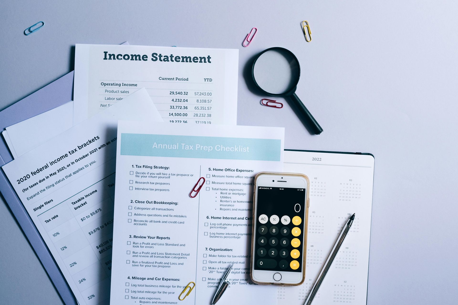 Financial documents with a calculator, magnifying glass, pen, and paperclips on a light gray surface.