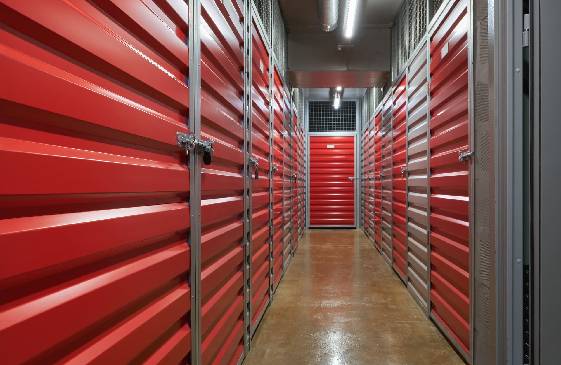 Indoor self storage hallway lined with red metal roll-up unit doors - Daphne, AL, East Bay Mini Storage