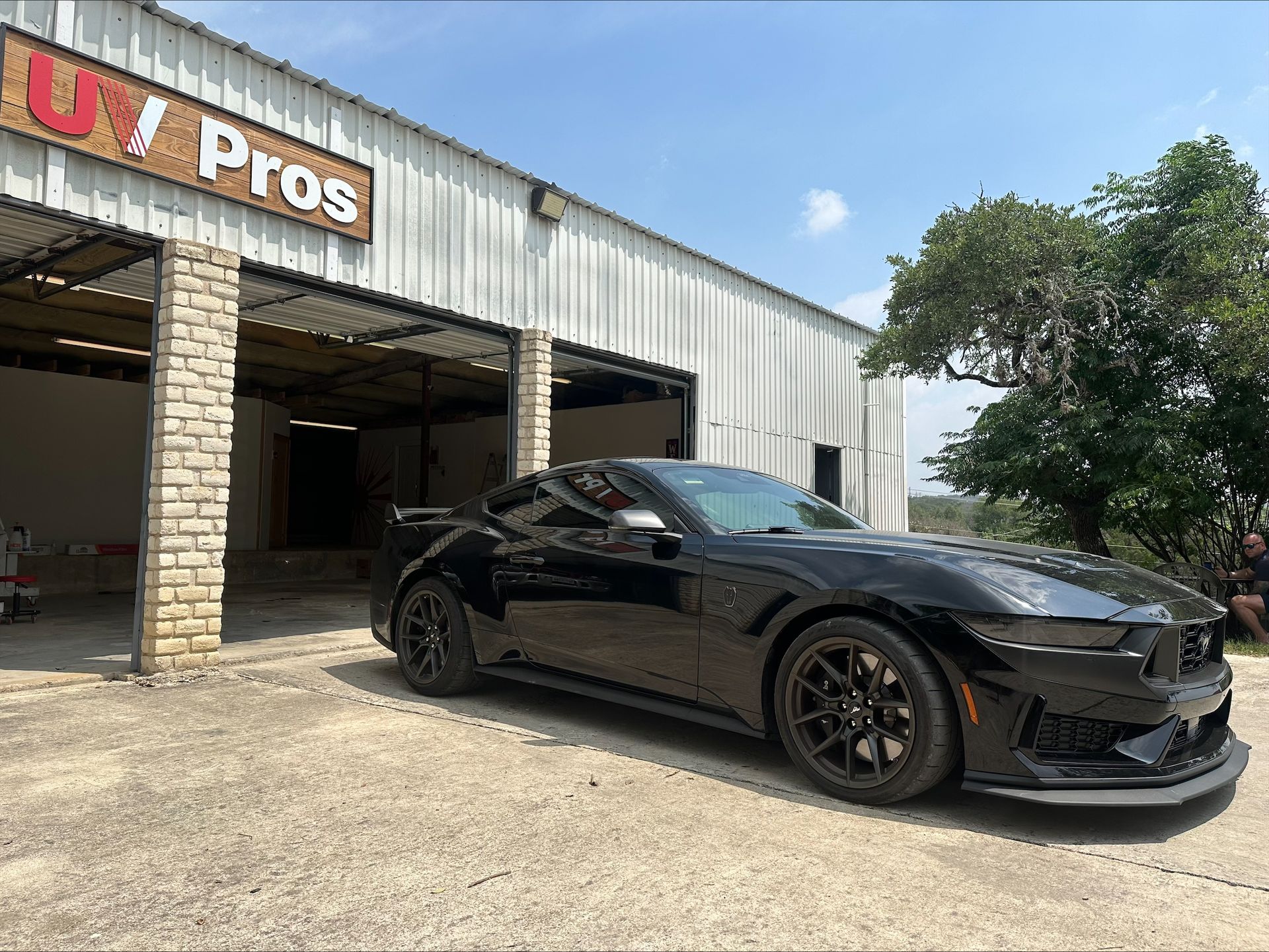 A black Ford Mustang sports car parked in front of a garage labeled 