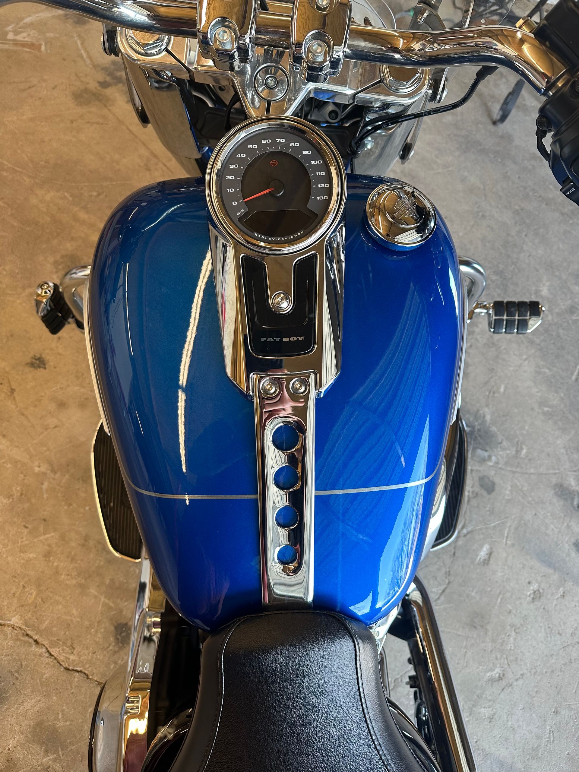 Top-down view of a blue motorcycle gas tank with a speedometer and chrome accents.