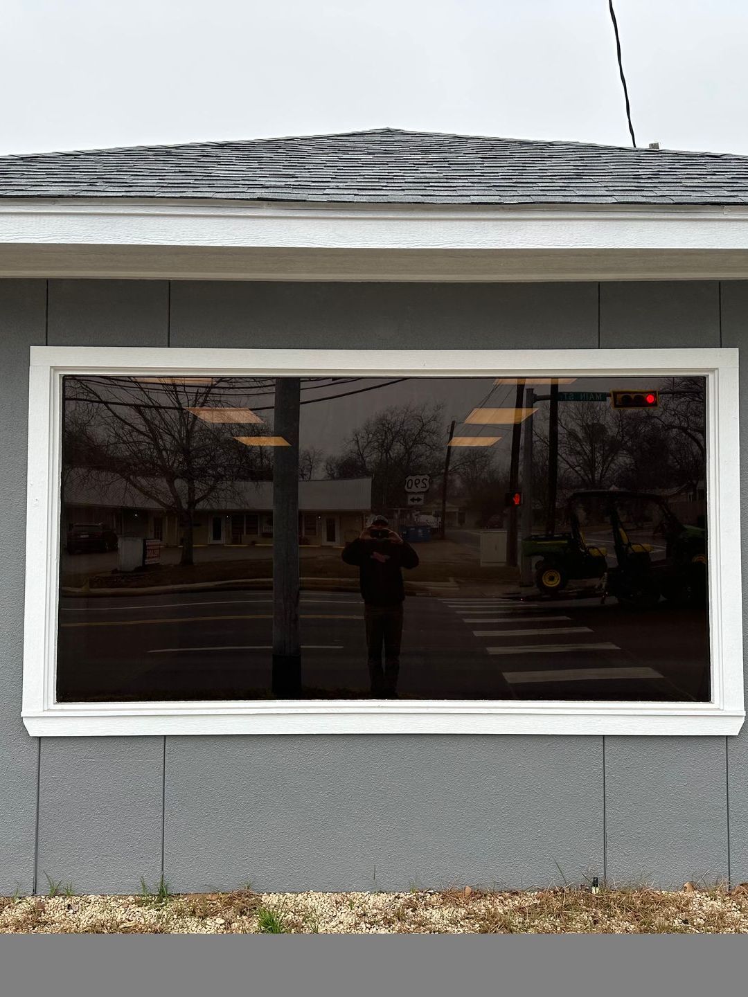 Exterior view of a building with a large window reflecting a person and a street scene under a cloudy sky.