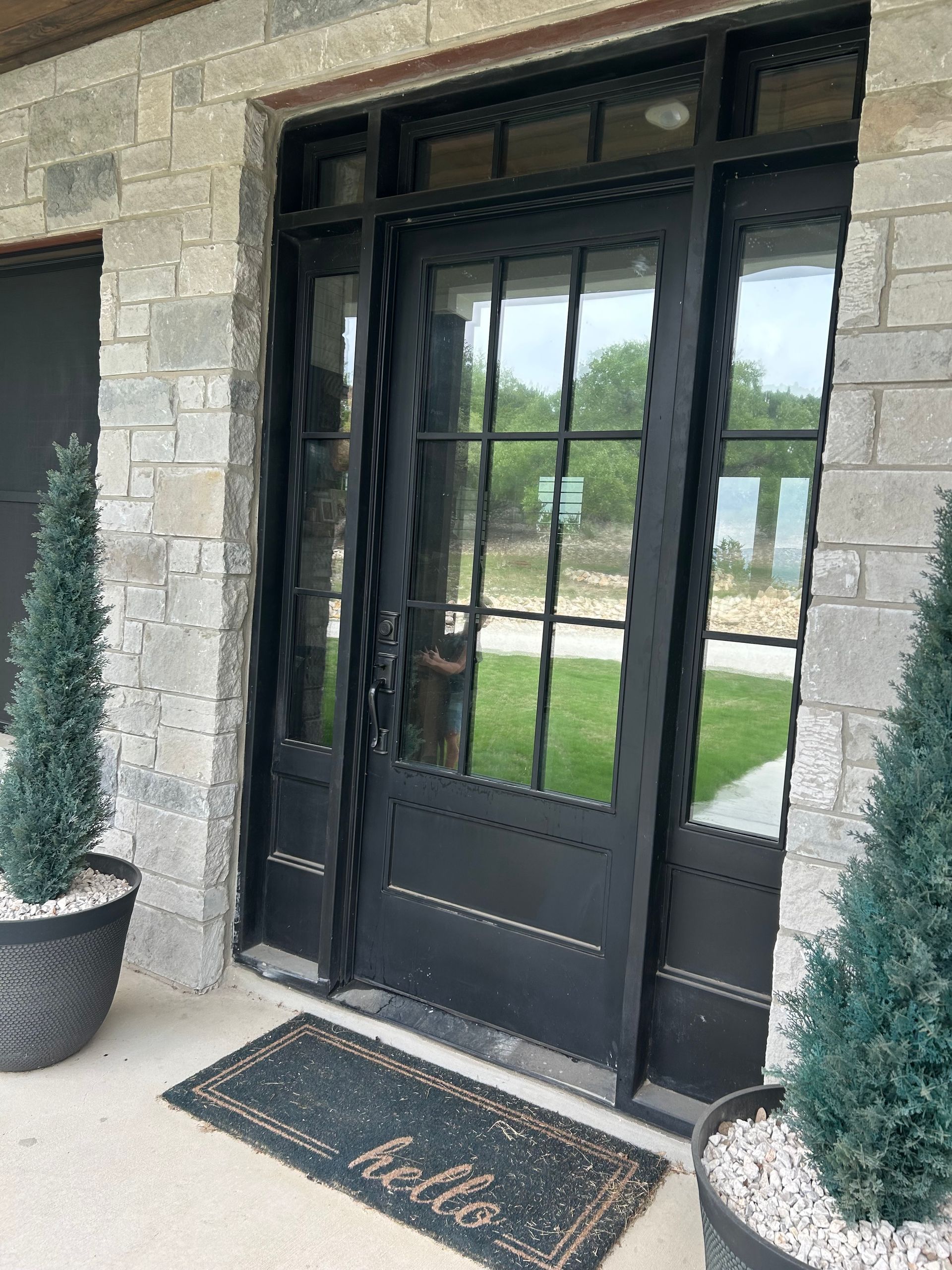 Black door with glass panes and side windows, in a stone frame, welcomes with a 