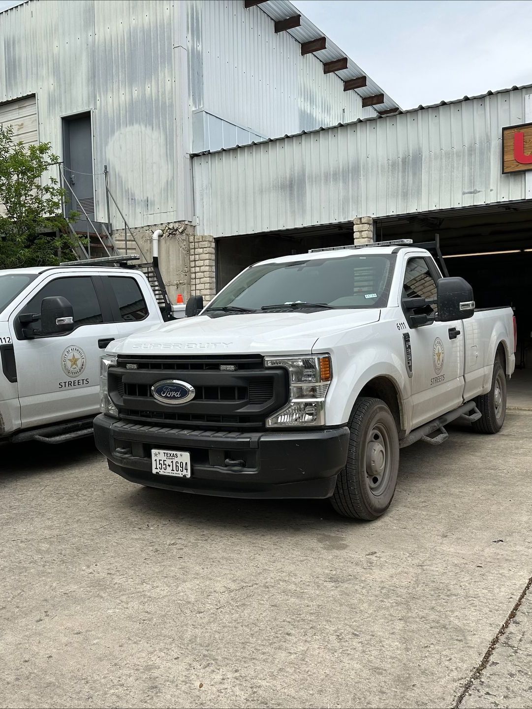 White Ford truck parked in front of a building. Another white truck is partially visible on the left. The setting appears to be outdoors.