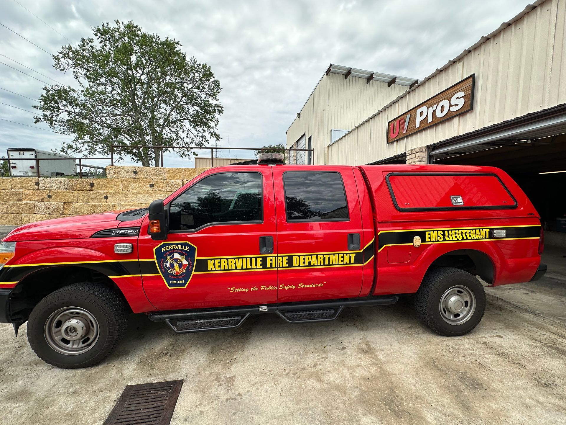 Red Kerrville Fire Department truck with black and gold accents parked near a building under an overcast sky.