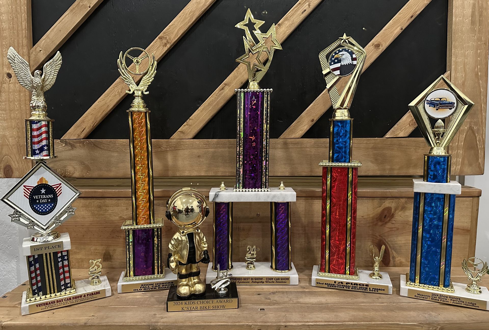Trophies on a wooden shelf, various shapes and sizes, with metallic gold and colorful columns.