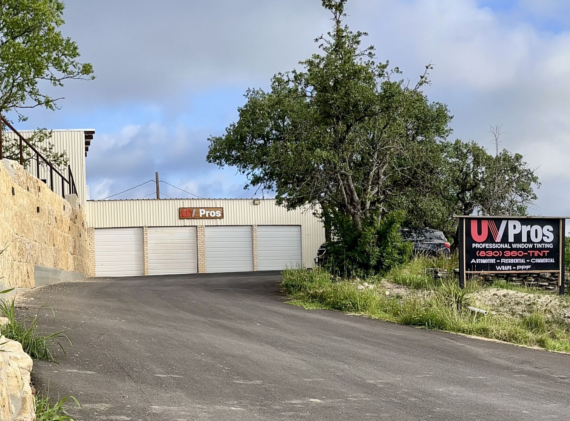 A building with large white doors and a sign for UV Pros, set on a sloped road with a natural, green environment.