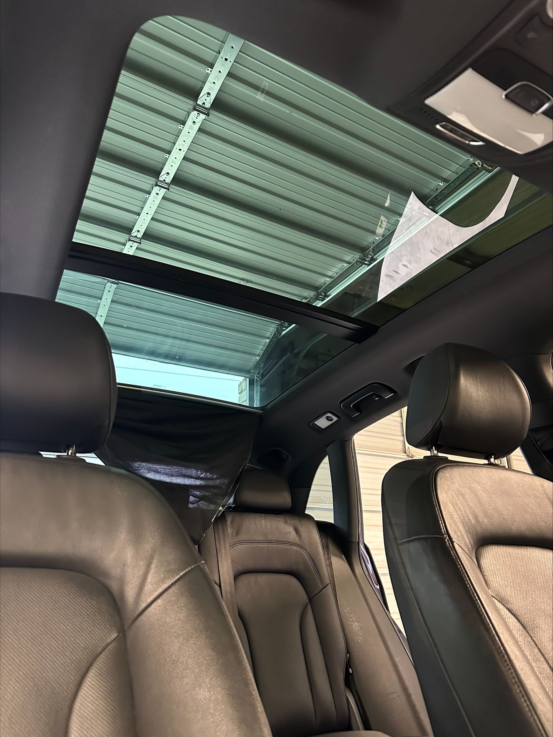 Interior of a car with a large panoramic sunroof, black leather seats, and a partially retracted sunshade.