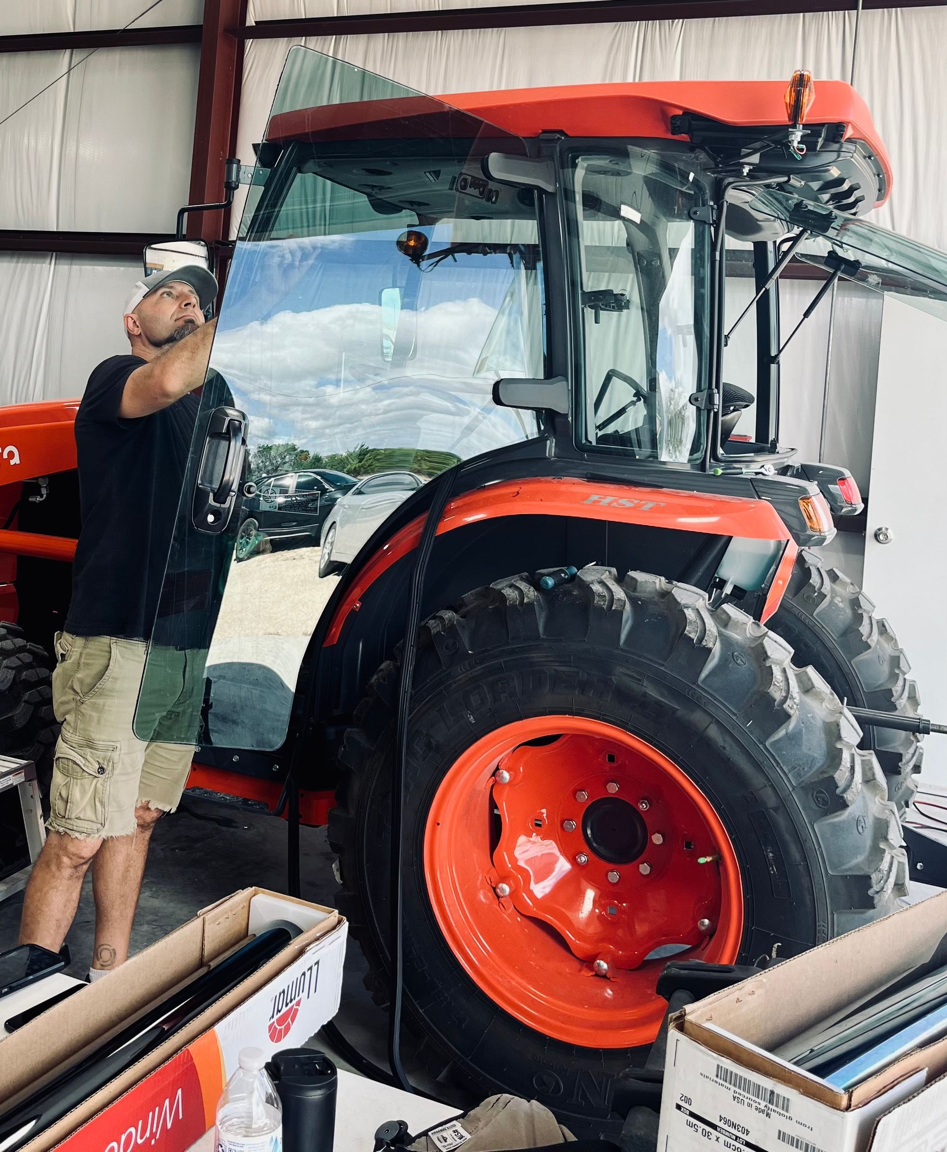 Man looking at a large orange tractor inside a warehouse. The tractor has a glass cab.