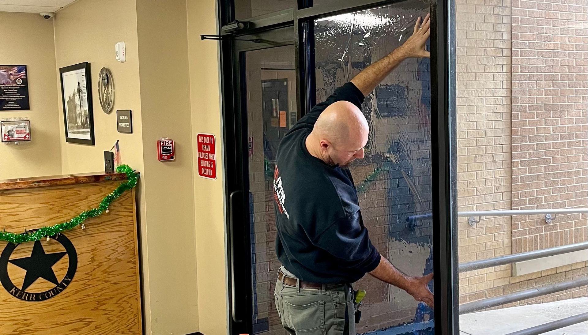 Man working on door. Building interior, festive decor. He's touching window.