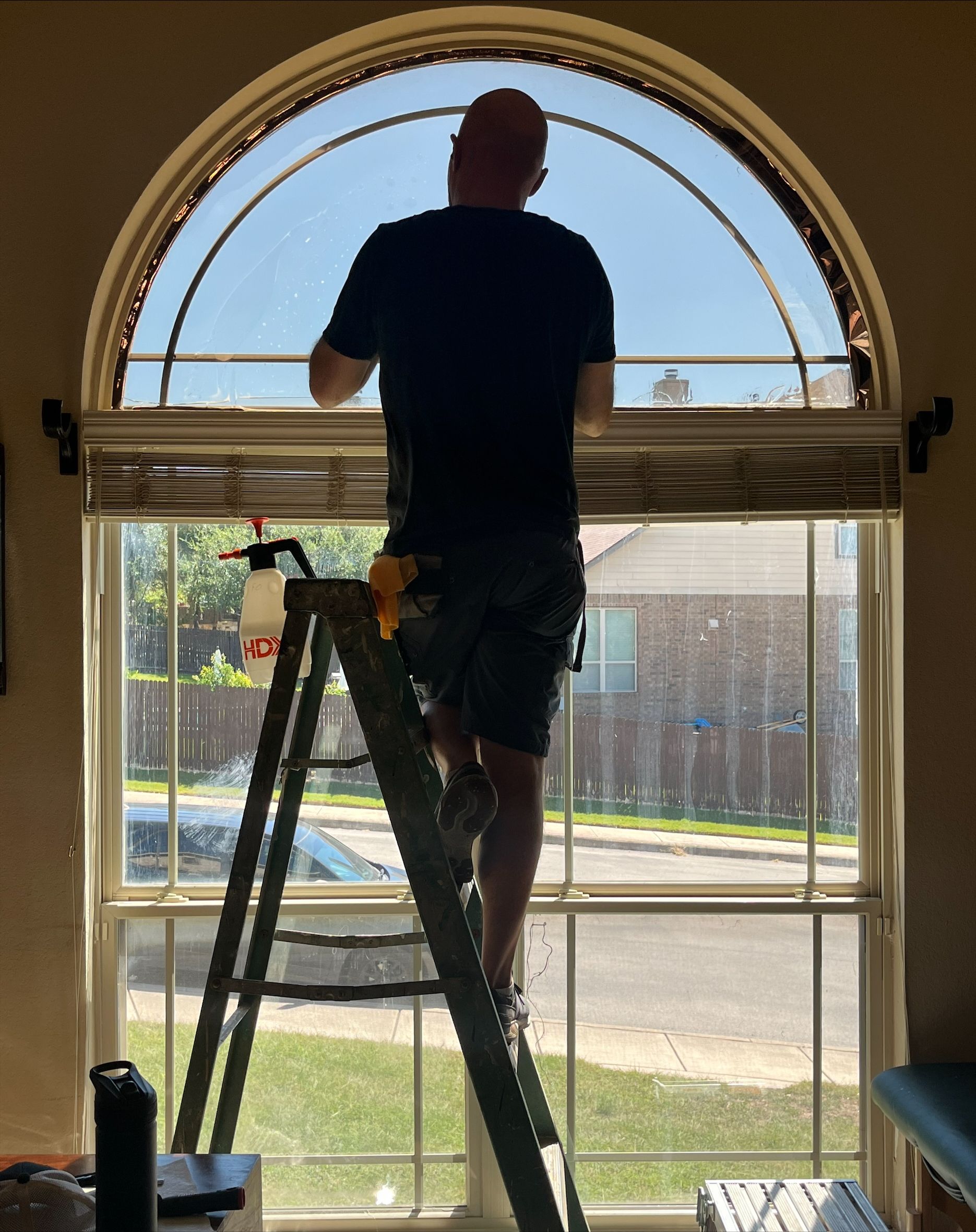 Person on a ladder cleaning a large arched window, indoors.