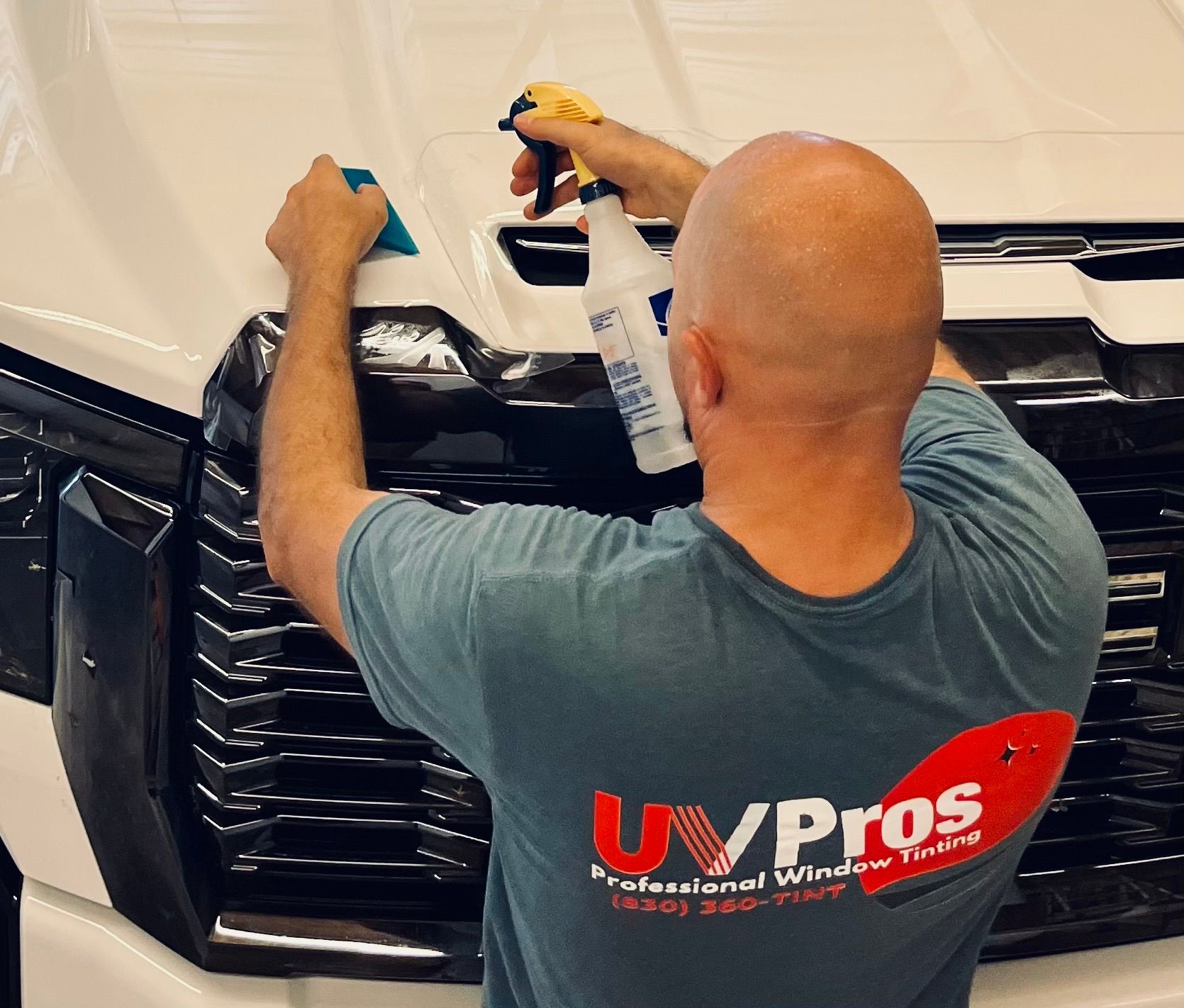 White SUV with one side covered in protective film in a garage. The rear windows are tinted.