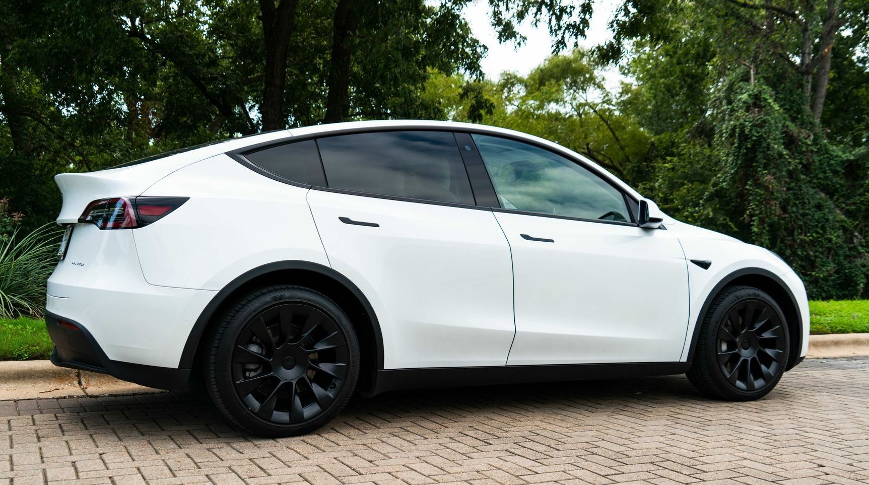 Person installing something on the roof of a white car, inside a garage. They're holding tools near the car's trim.