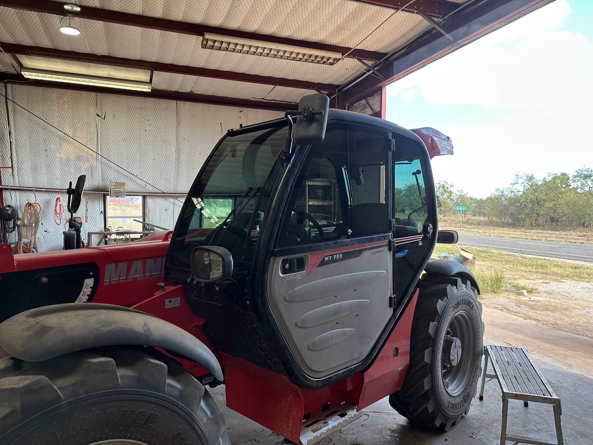 Man using a heat gun to apply film to a black car's window in a garage.