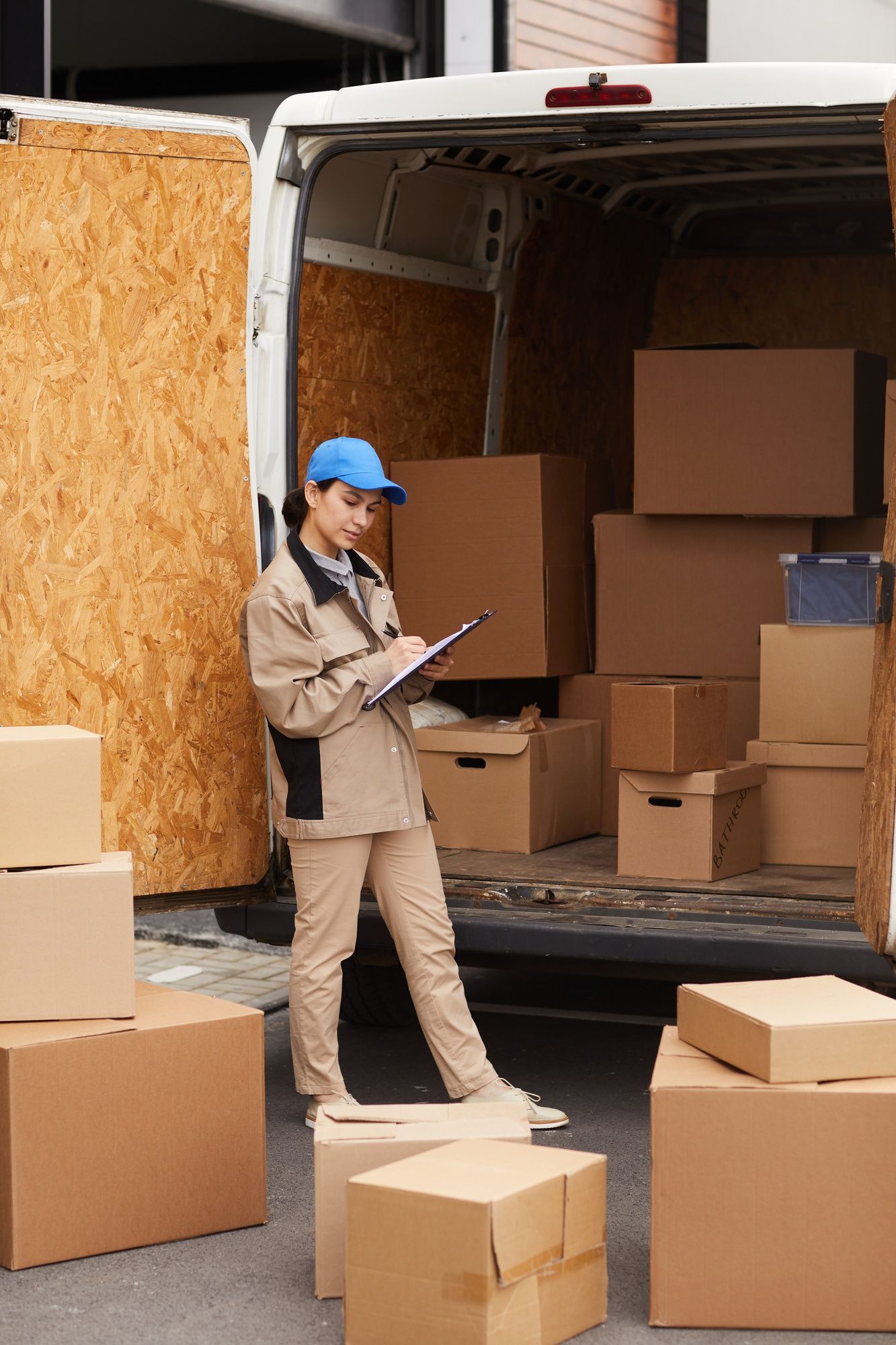 A delivery woman is standing in front of a van filled with cardboard boxes.