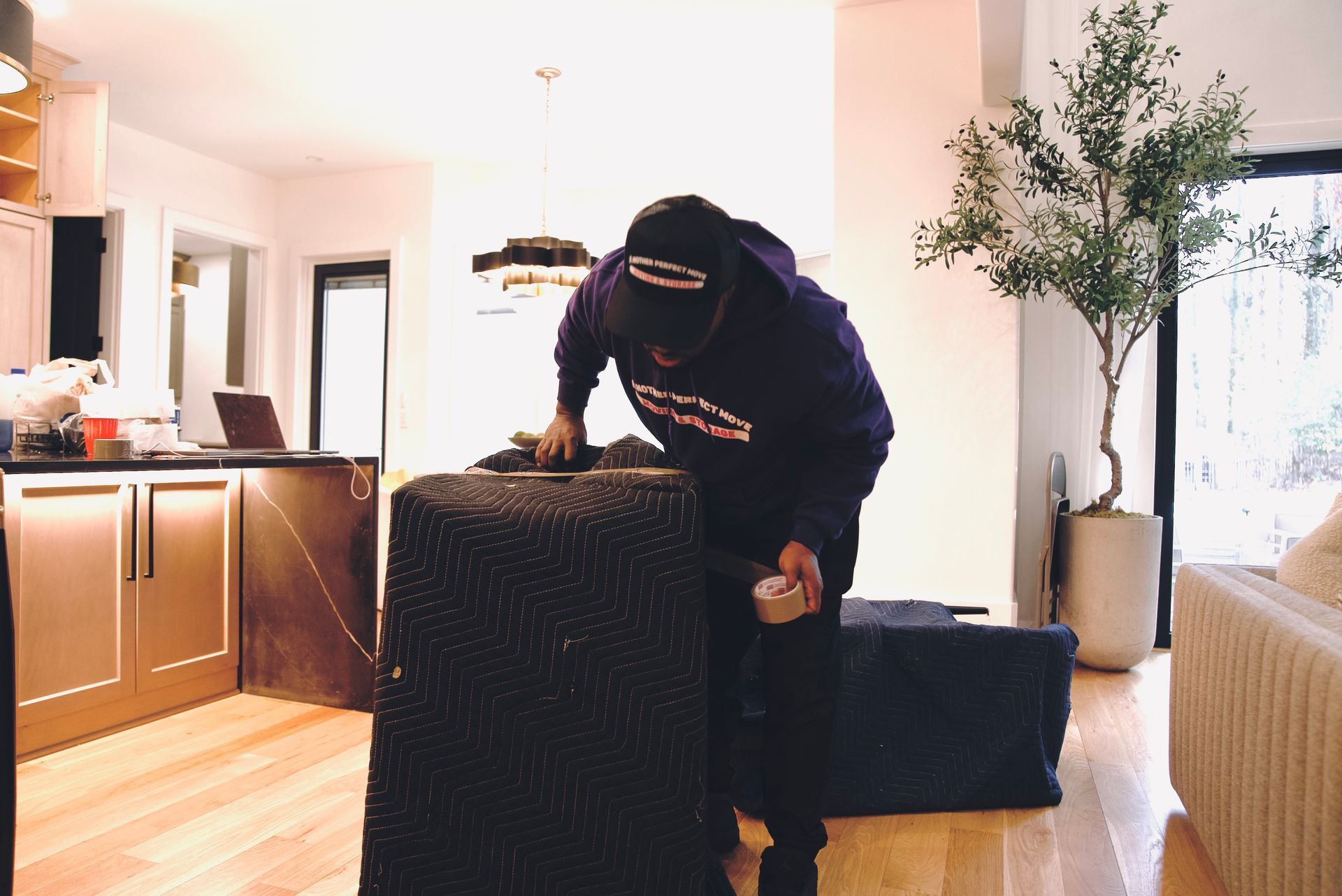 A man in a purple hoodie is standing next to a couch in a living room.