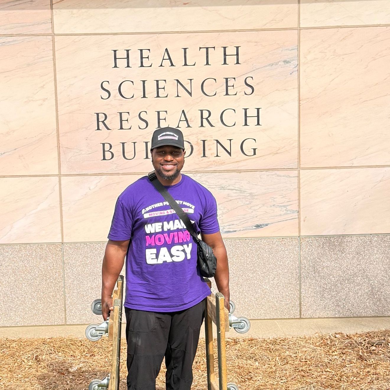 A man in a purple shirt is standing in front of the health sciences research building