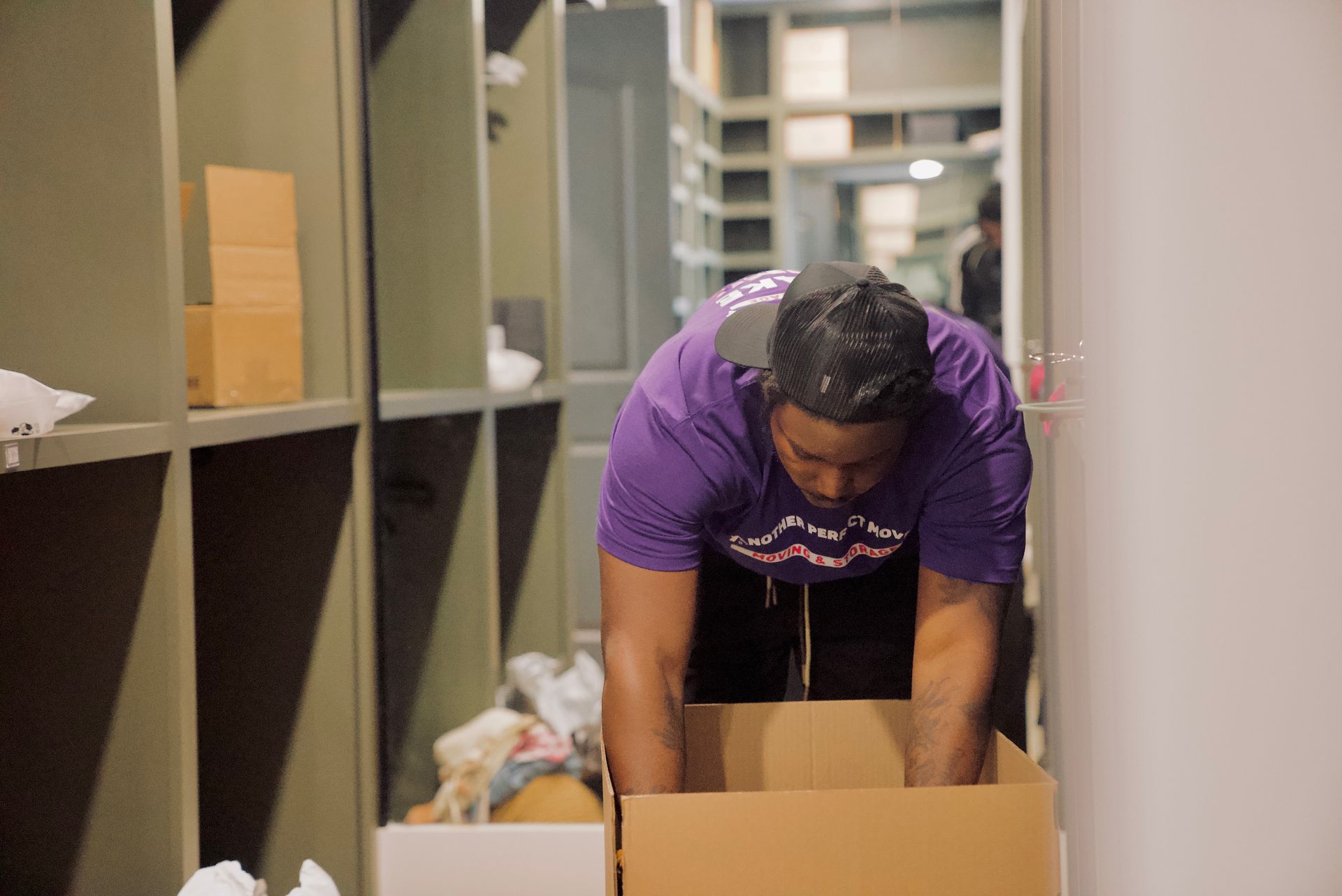 Person in purple shirt packing a box in a storage room with shelves.
