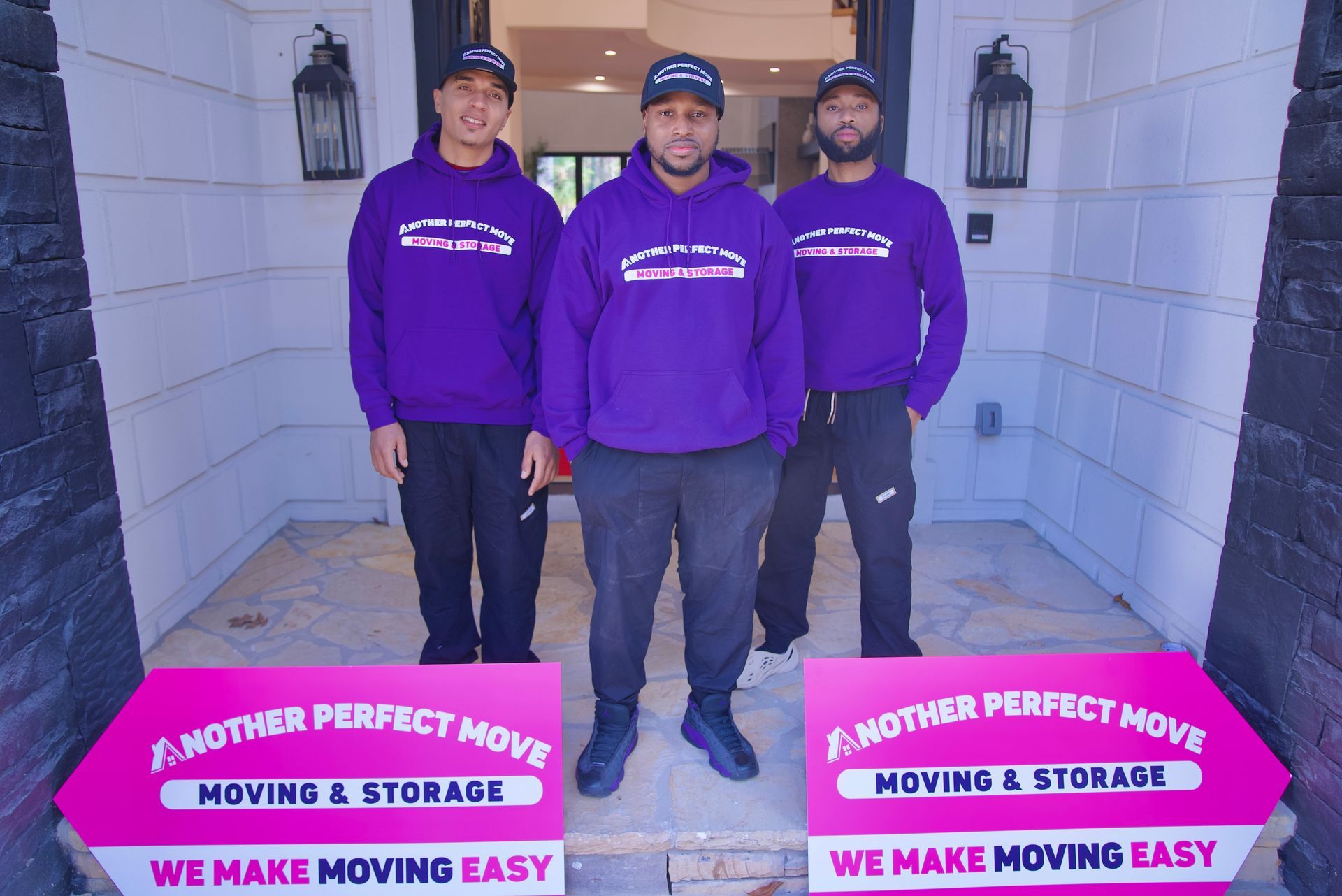 Three men wearing purple sweatshirts are standing next to each other in front of a house.