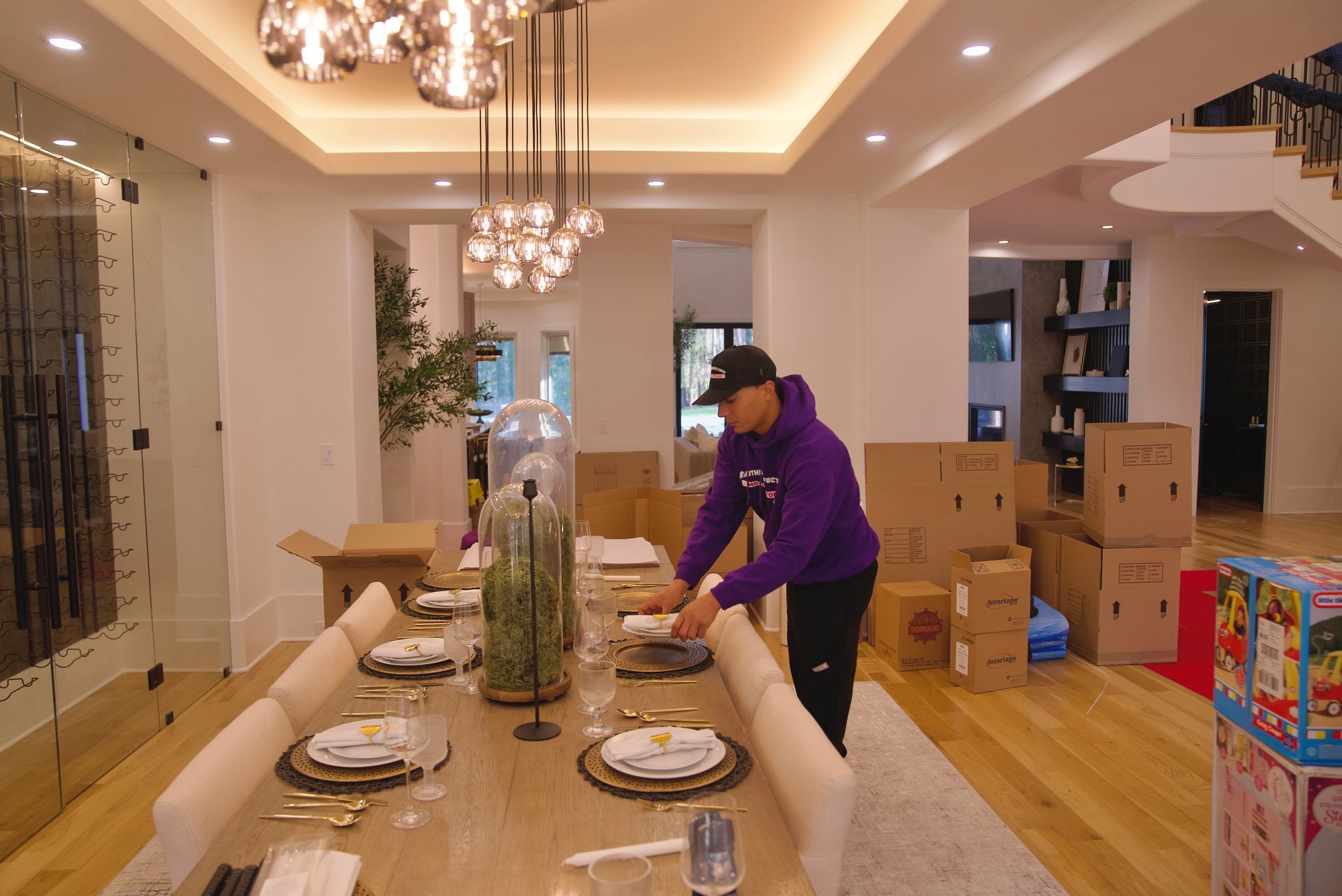 A man in a purple hoodie is setting a table in a dining room.