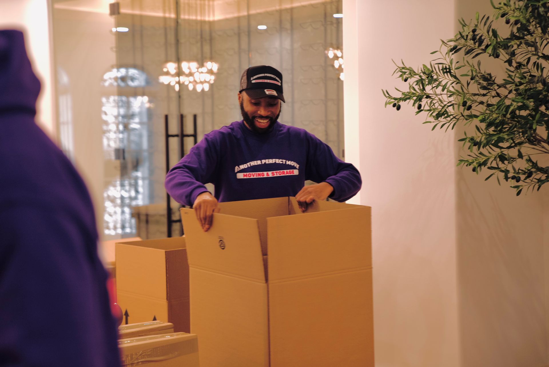 A man in a purple shirt is holding a cardboard box.