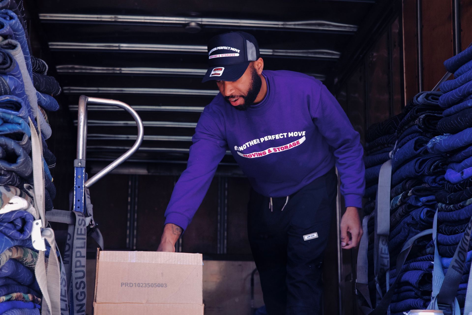 A man in a purple shirt is loading a box into a truck.