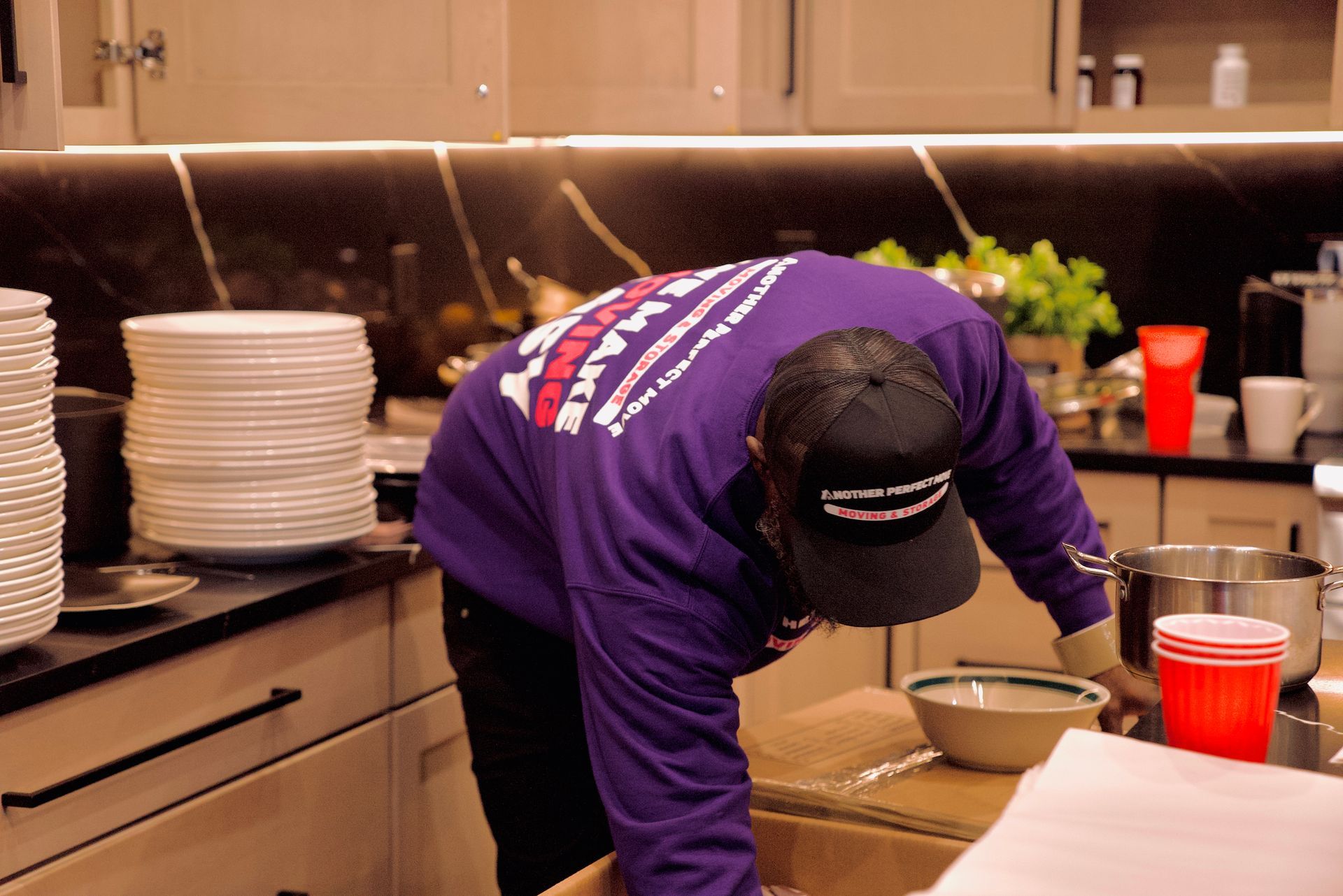 A man in a purple shirt is bending over in a kitchen.