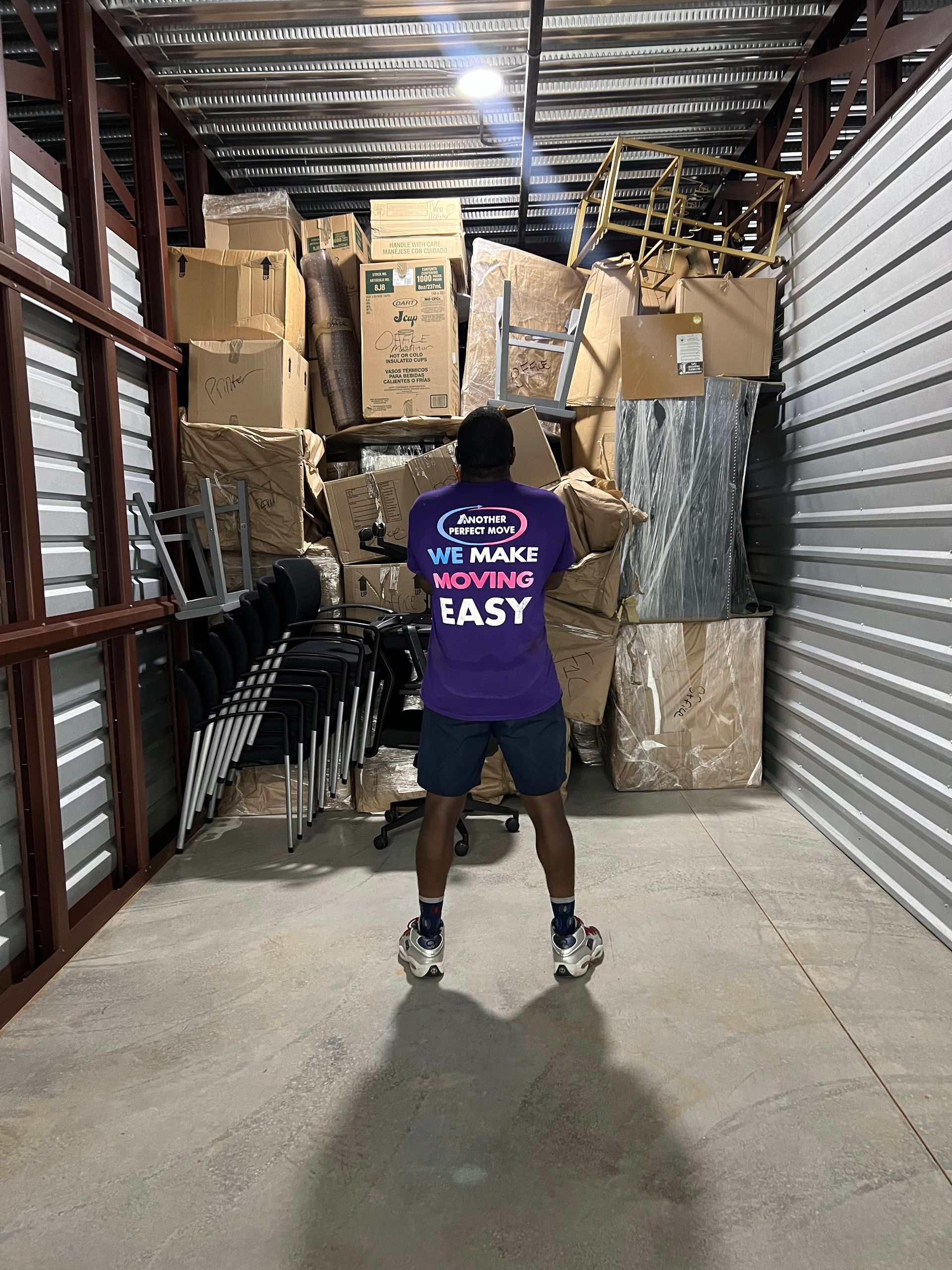 A man in a purple shirt is standing in a warehouse filled with boxes.