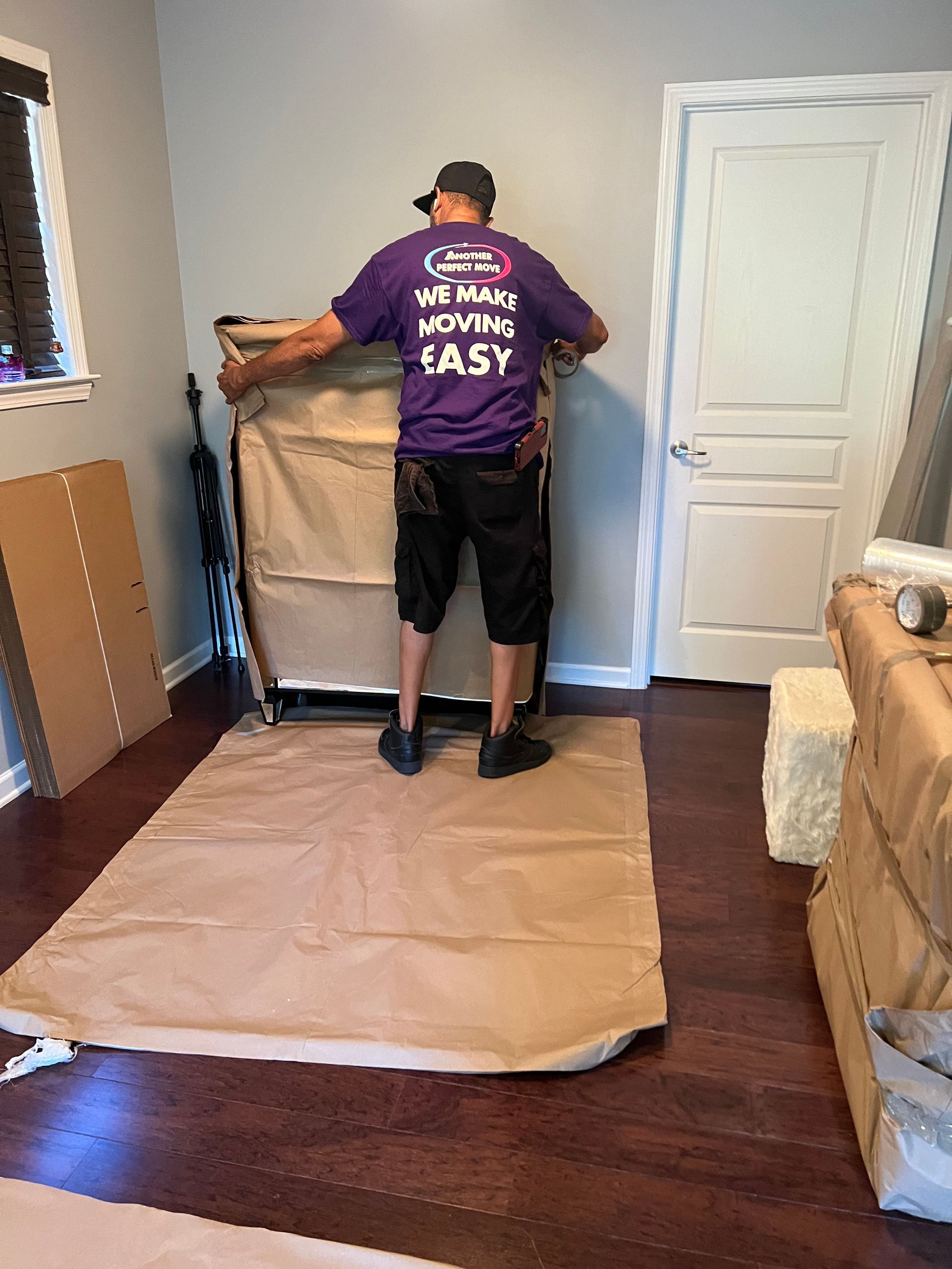 A man in a purple shirt is moving a couch in a room.