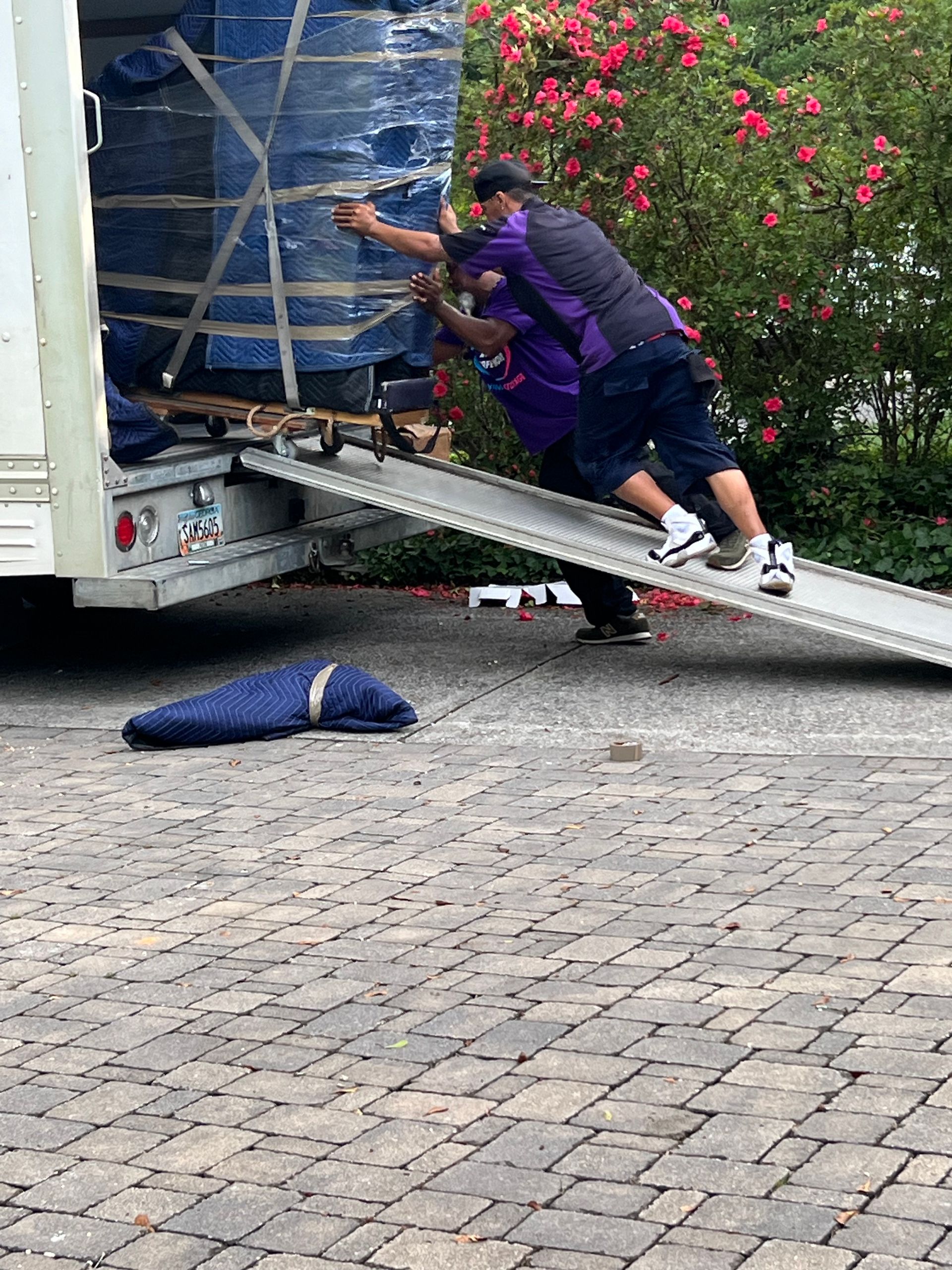 Two men are pushing a moving truck down a ramp.