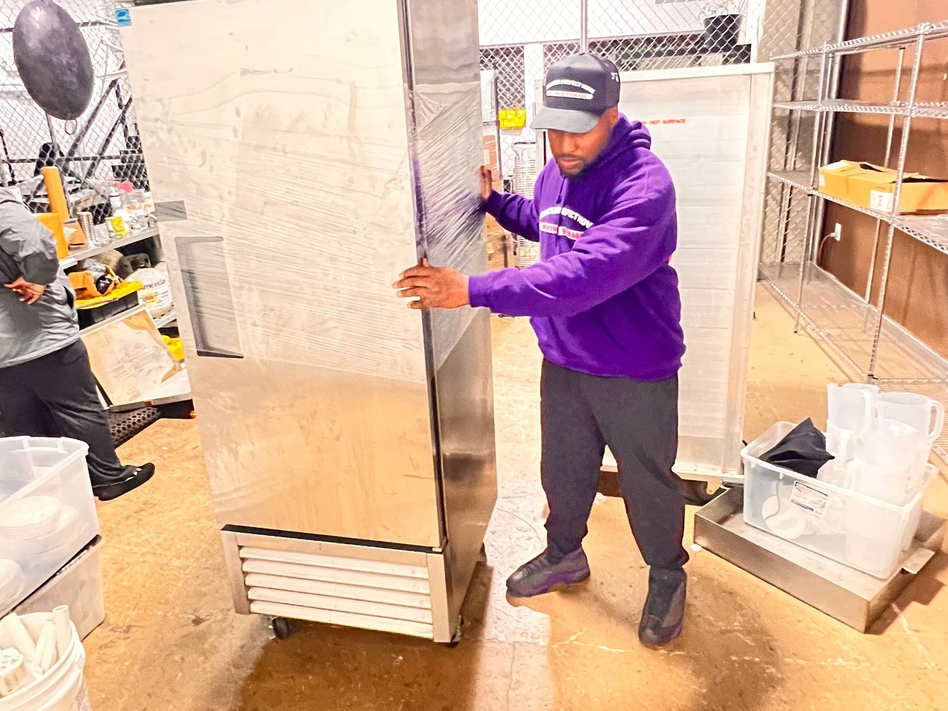 A man in a purple hoodie is pushing a refrigerator in a kitchen.
