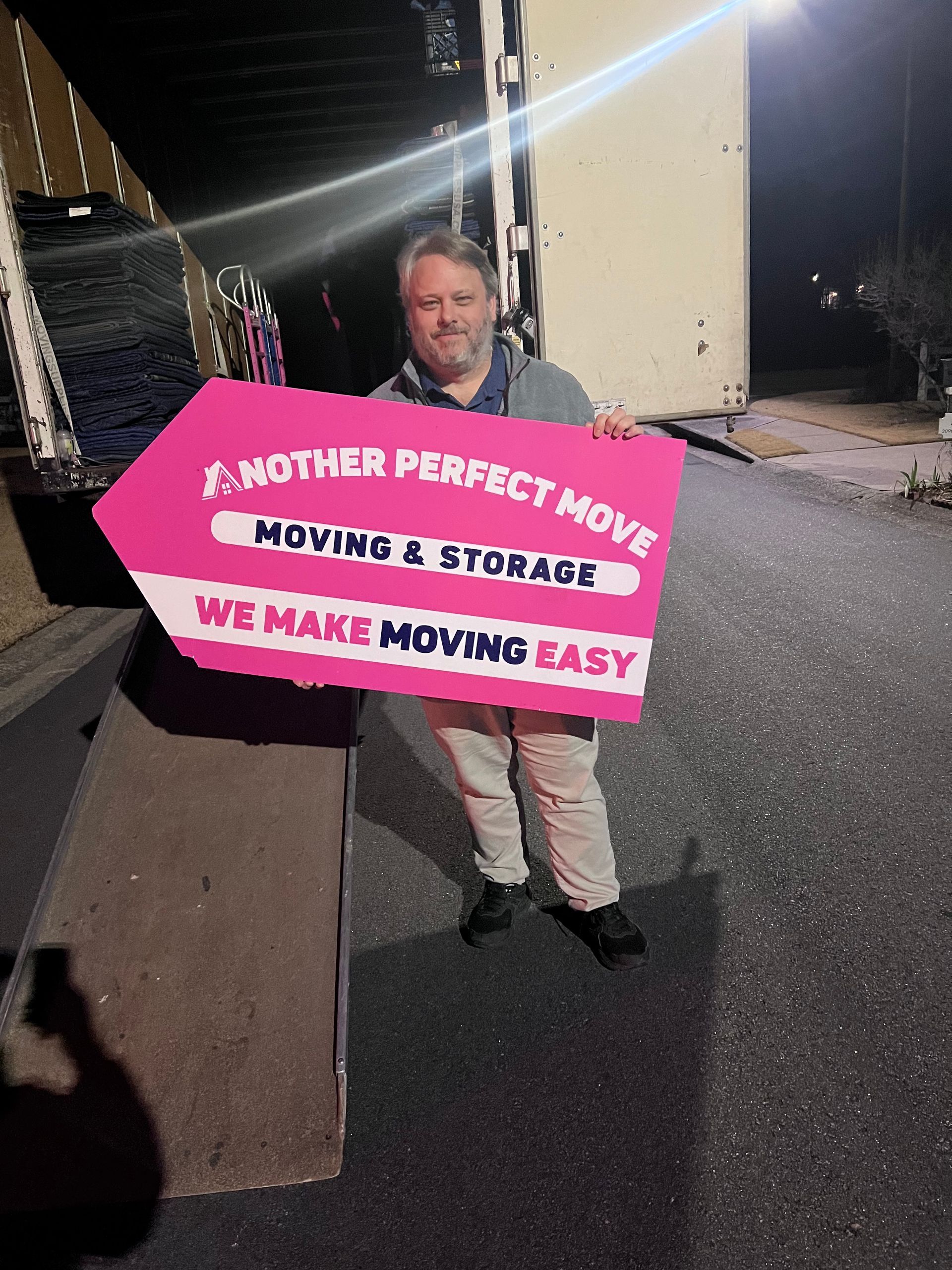 A man is holding a sign that says another perfect move moving & storage