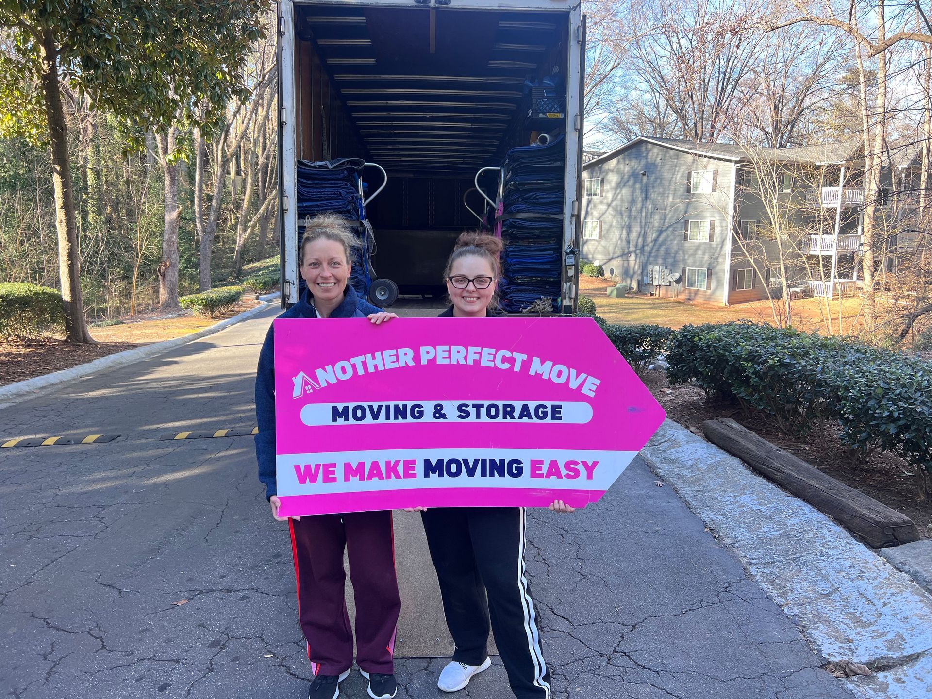 Two women are holding a sign in front of a moving truck.