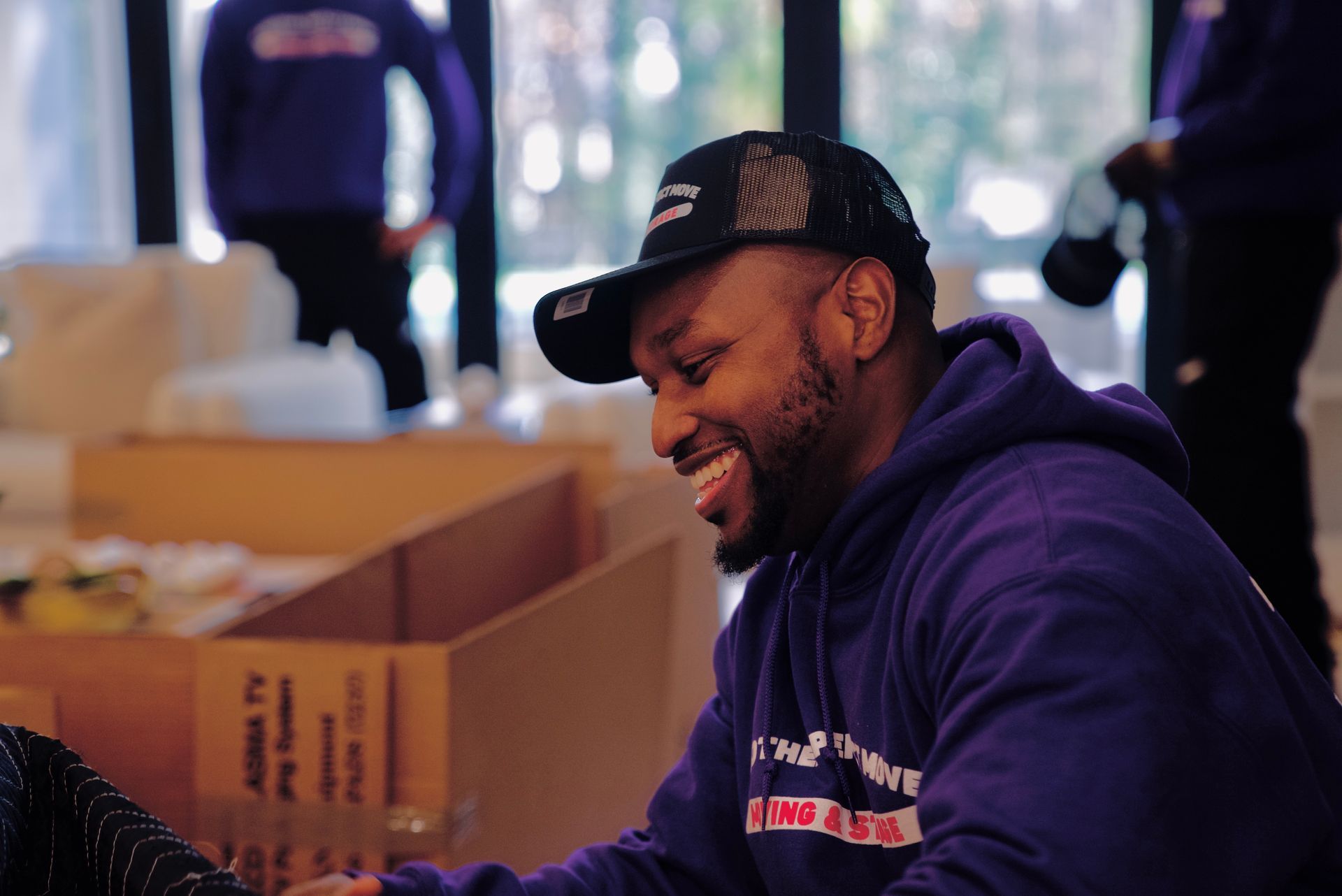 A man wearing a purple hoodie and a black hat is smiling.