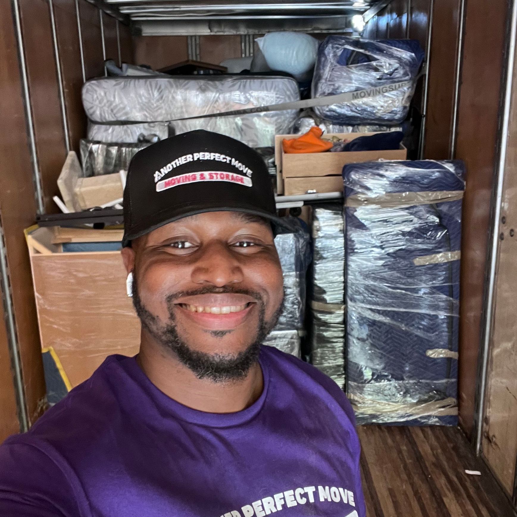 A man wearing a purple shirt and a black hat is standing in a moving truck.