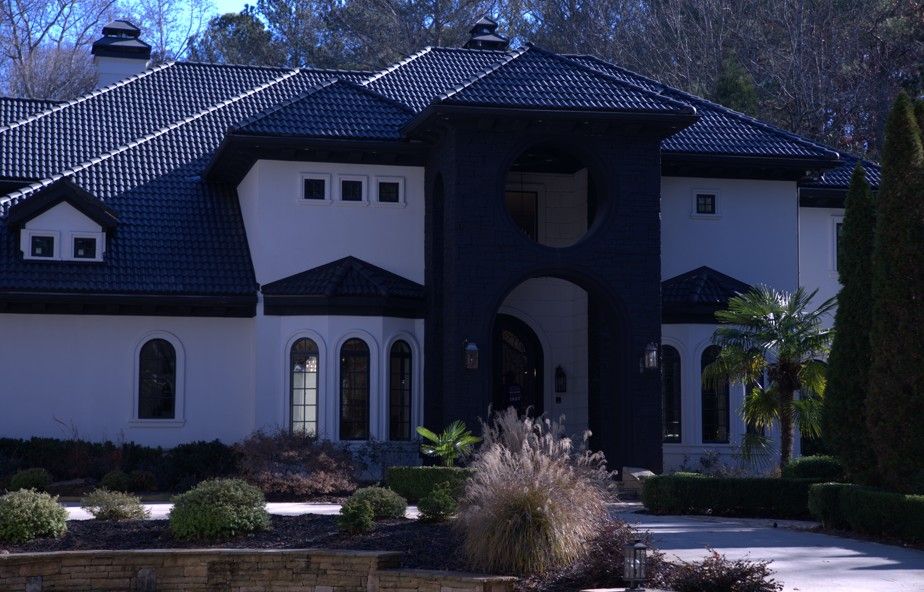 Two-story house with black roof and trim, white exterior. Landscaping with bushes and plants in front.