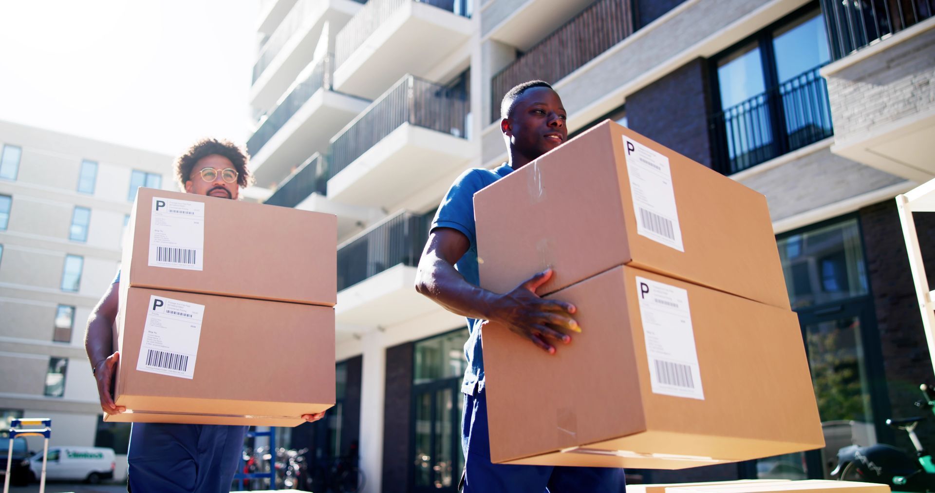 Two men are carrying boxes in front of a building.