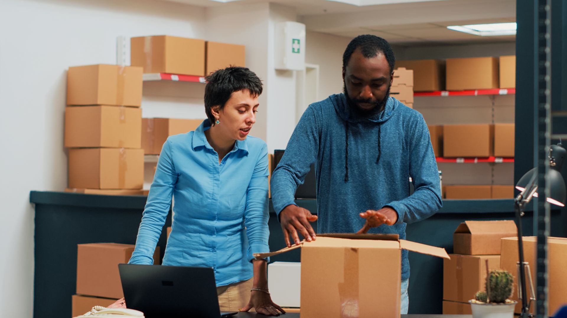 A man and a woman are standing next to each other in an office looking at a cardboard box.