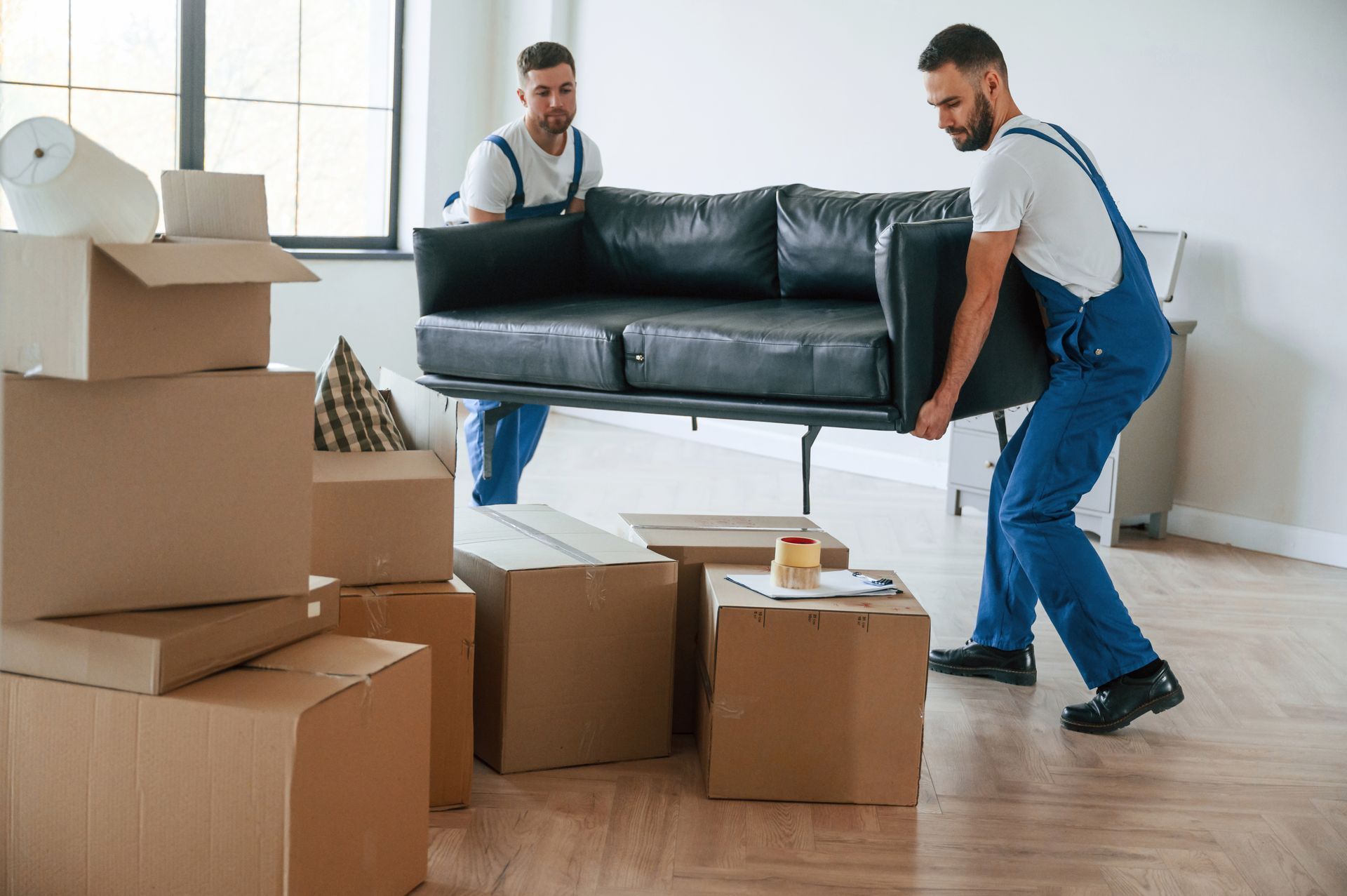 Two men are carrying a couch in a living room.