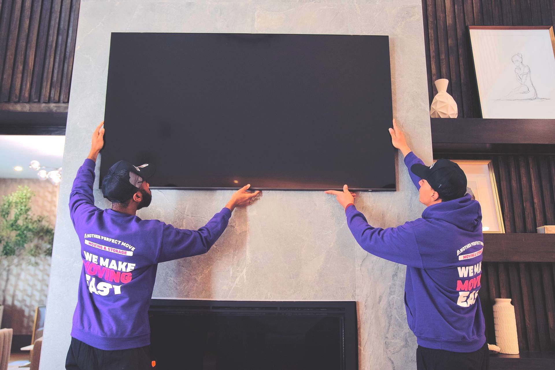 Two men are installing a flat screen tv on a wall.