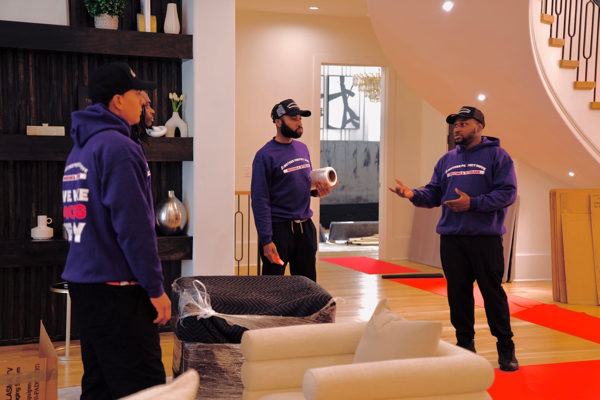 Three men in purple sweatshirts are standing in a living room.