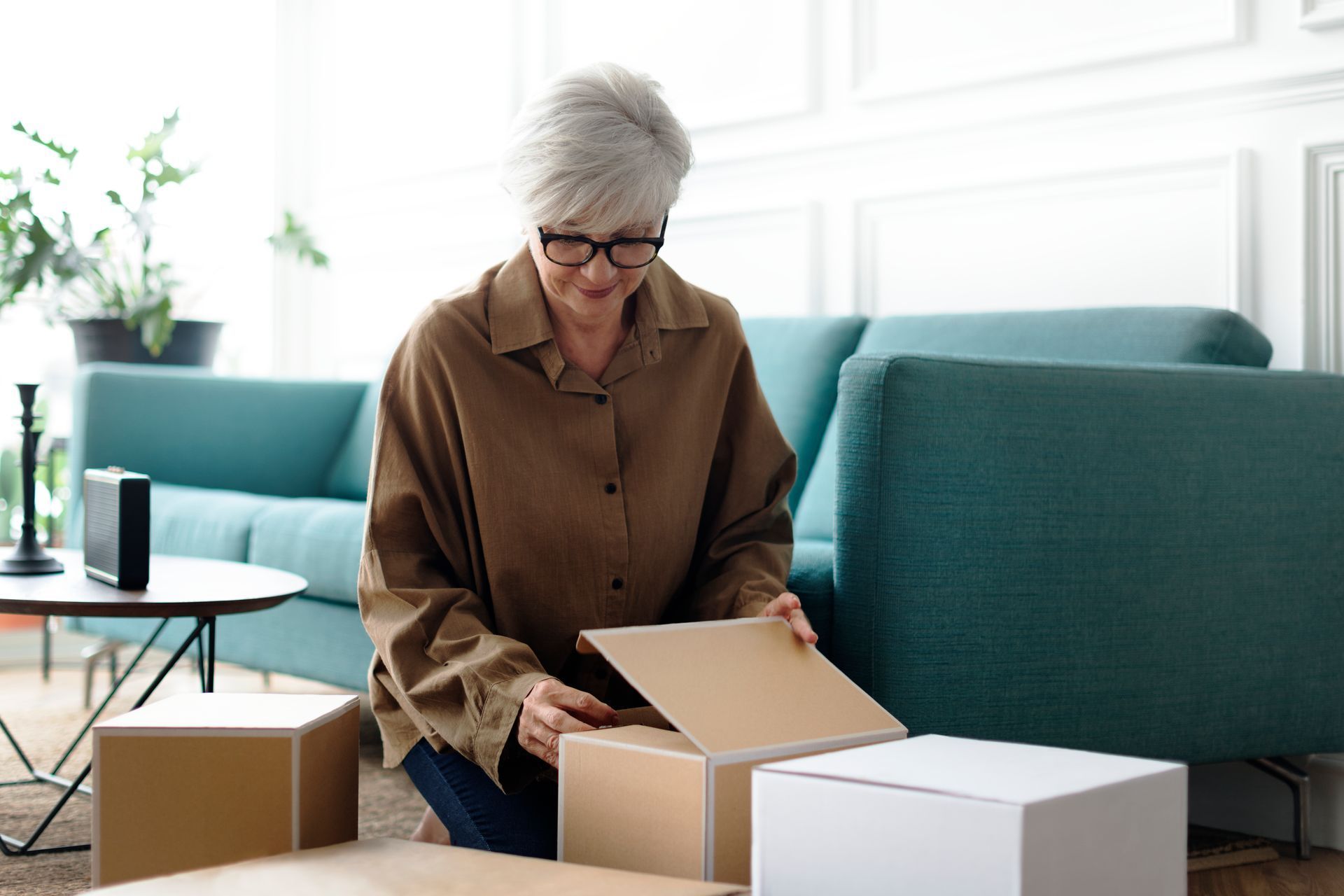 A woman is sitting on the floor in a living room holding a cardboard box.