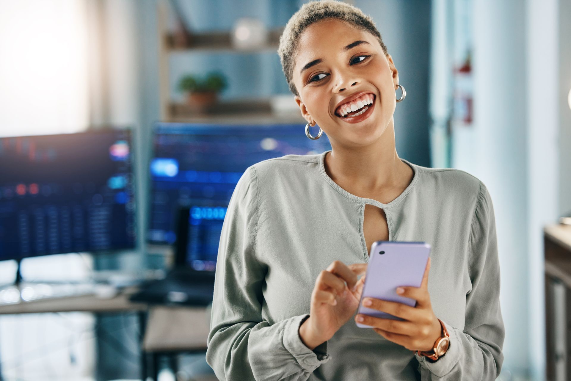 A woman is smiling while holding a cell phone.