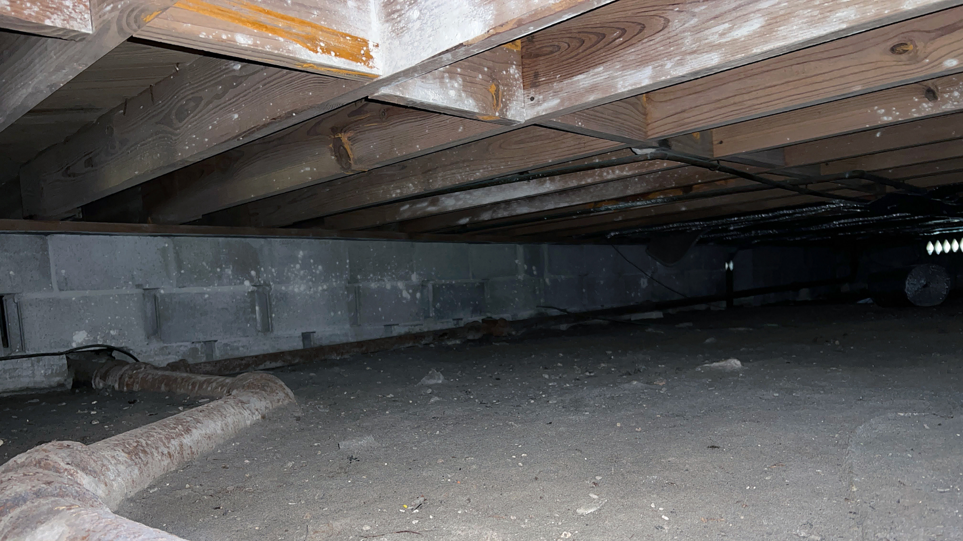 Crawl space with wooden beams, cinder block foundation, and dirt floor.