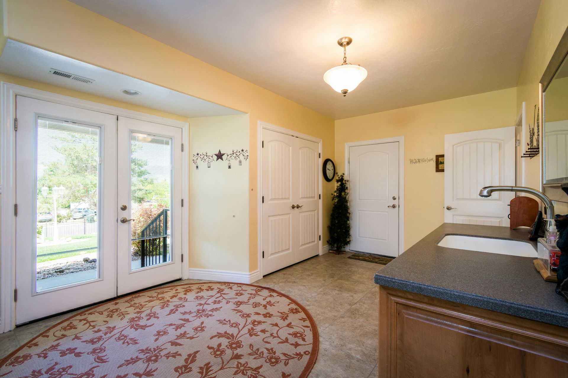 Bright entryway with doors to the outside and a small sink area, featuring a round patterned rug.